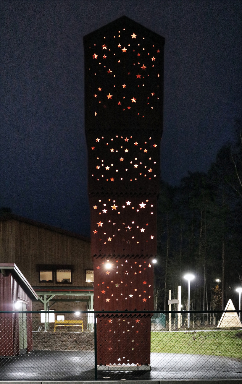 The sculpture of stacked houses in the school yard at UMA is illuminated by cut-out stars