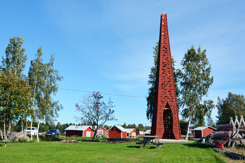 El faro rojo de la pirámide de madera de Ulf Mejergren brilla a través de cortes de pescado en la isla báltica