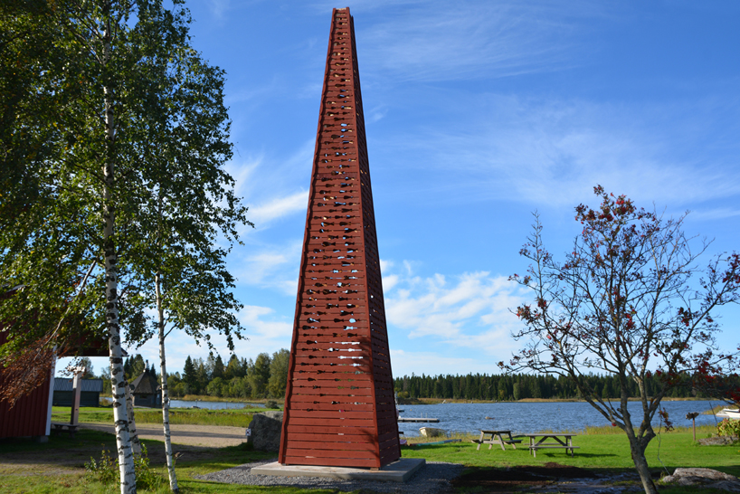 El faro rojo de la pirámide de madera de Ulf Mejergren brilla a través de cortes de pescado en la isla báltica