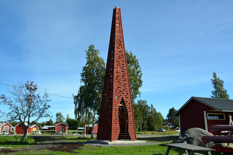 El faro rojo de la pirámide de madera de Ulf Mejergren brilla a través de cortes de pescado en la isla báltica