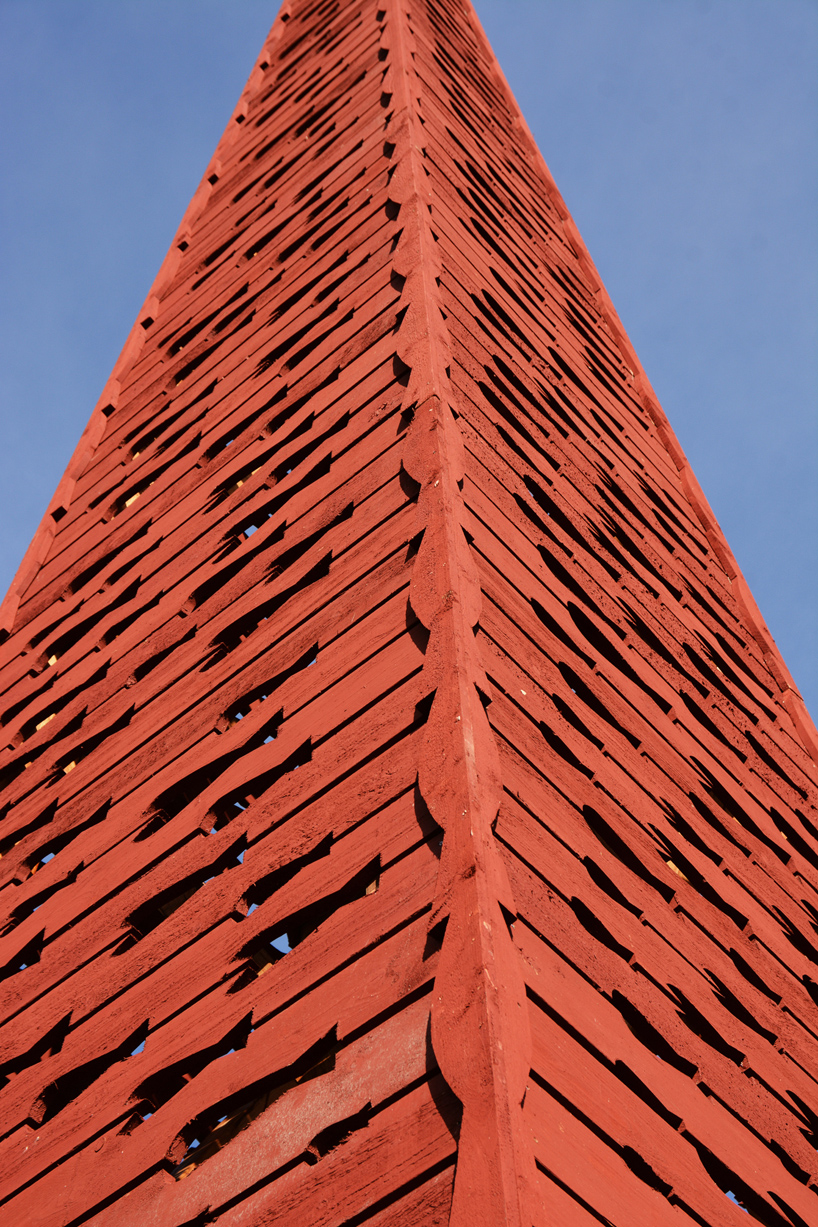 El faro rojo de la pirámide de madera de Ulf Mejergren brilla a través de cortes de pescado en la isla báltica