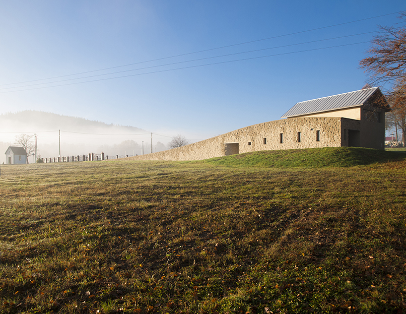 a delicate arched wall rises from the ground to embrace the 'chapel of the last farewell' in poland