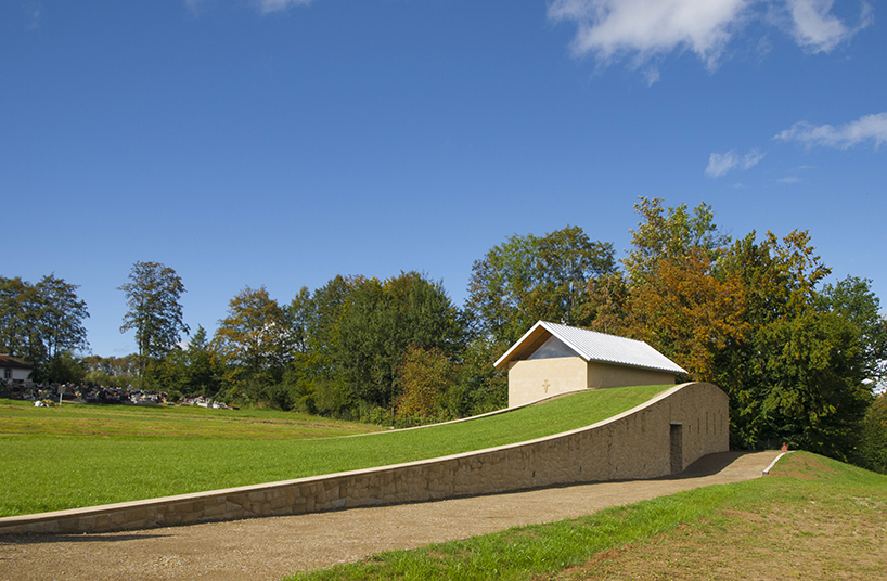 a delicate arched wall rises from the ground to embrace the 'chapel of the last farewell' in poland