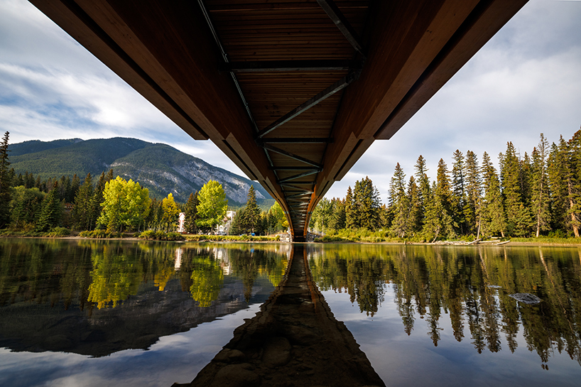 nancy pauw pedestrian bridge's timber arch spans over bow river in canada