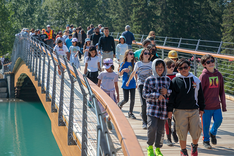 nancy pauw pedestrian bridge's timber arch spans over bow river in canada