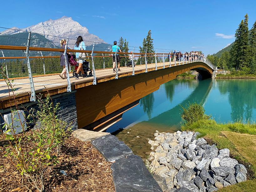 nancy pauw pedestrian bridge's timber arch spans over bow river in canada