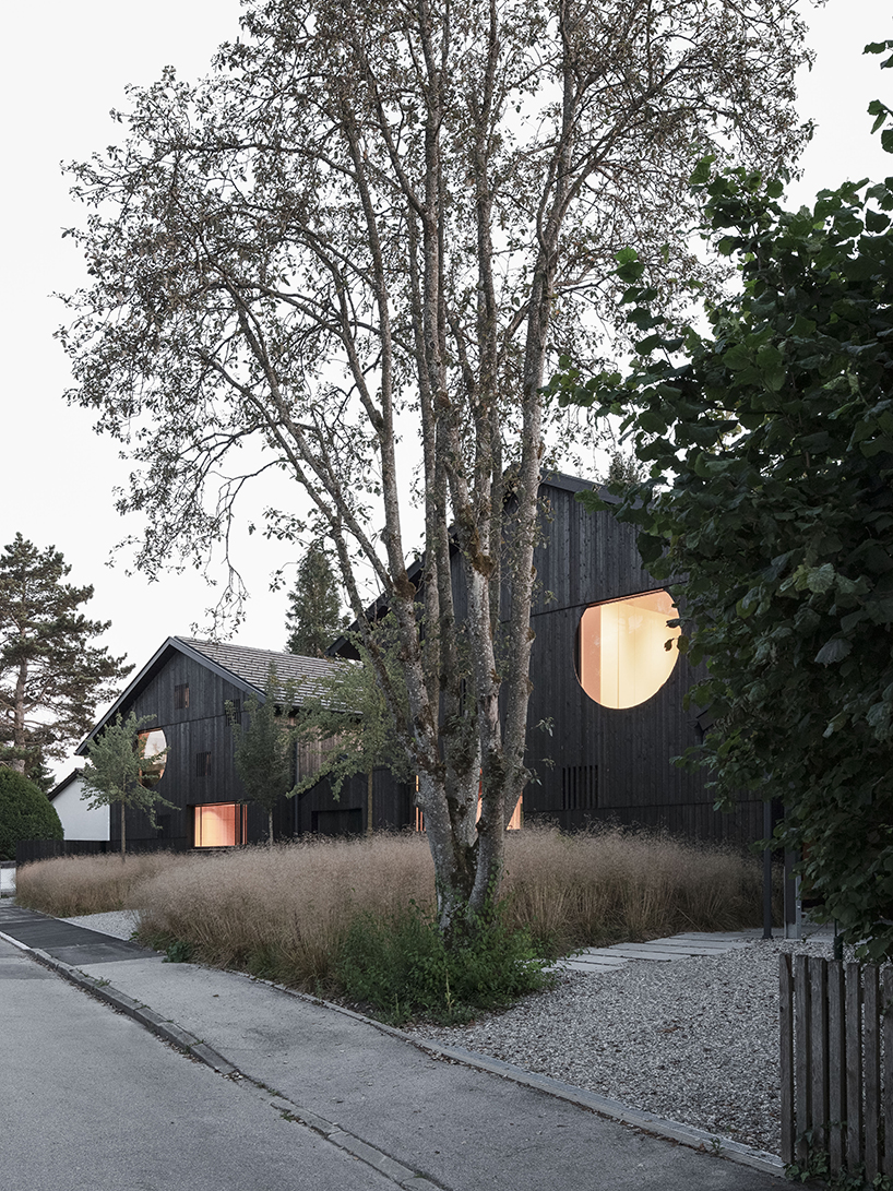 black charred timber cladding envelops twin gabled houses with one pillar in munich