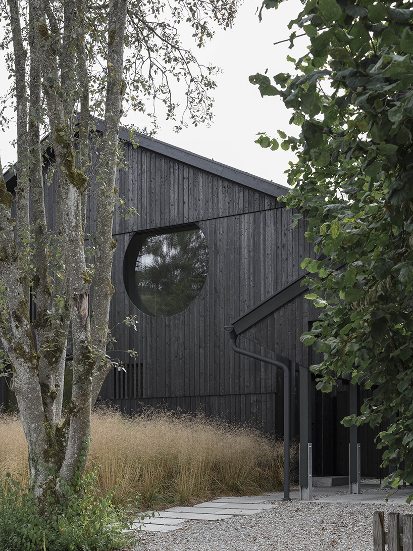 black charred timber cladding envelops twin gabled houses with one pillar in munich