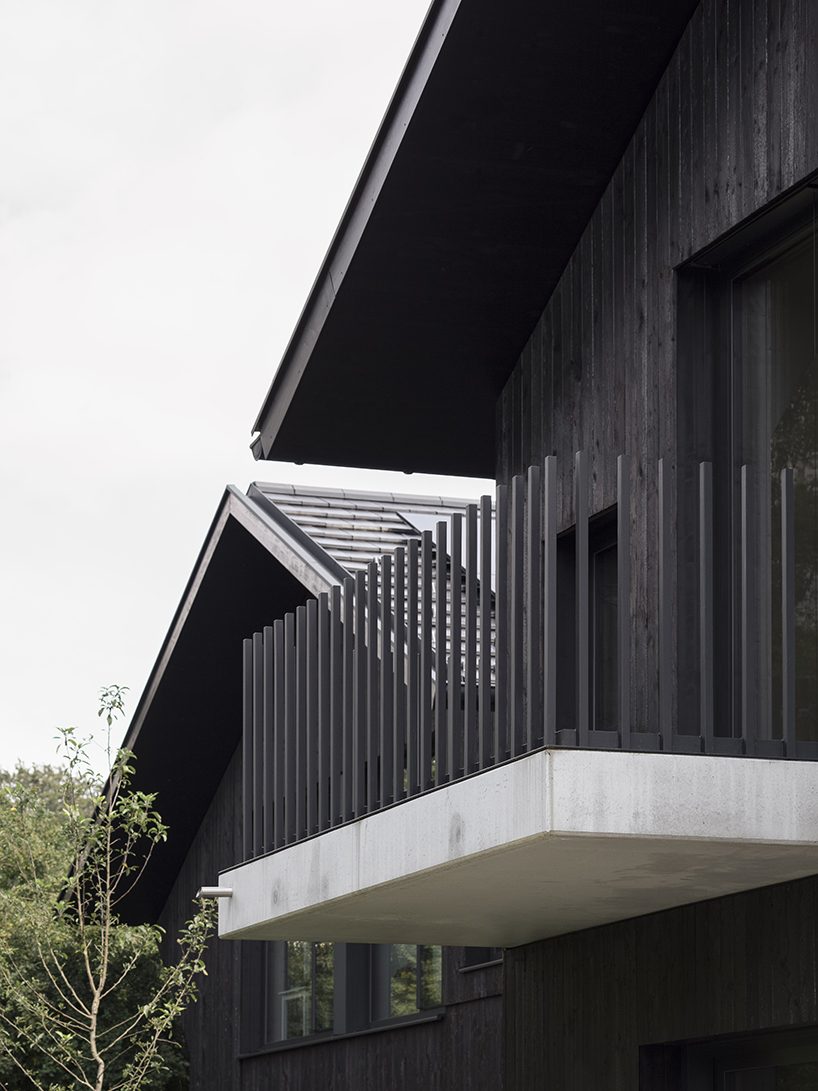 black charred timber cladding envelops twin gabled houses with one pillar in munich