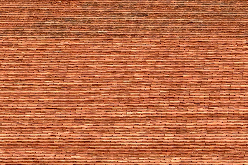 clad in terracotta tiles, morjor café floats above water pond in thailand