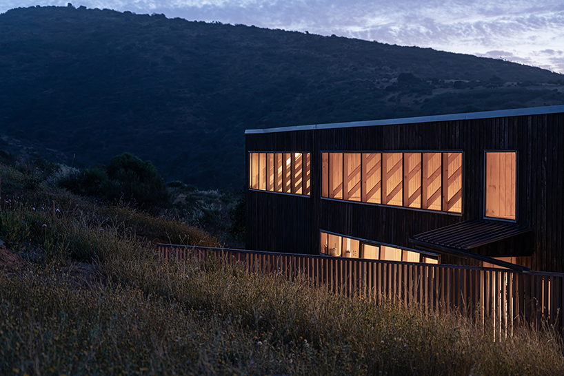 charred timber wraps linear casa las tupas, topped with pitched roof in northern chile