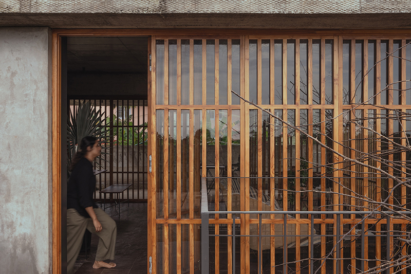 hybrid office-residence extends raw concrete balcony above recessed timber mass in india