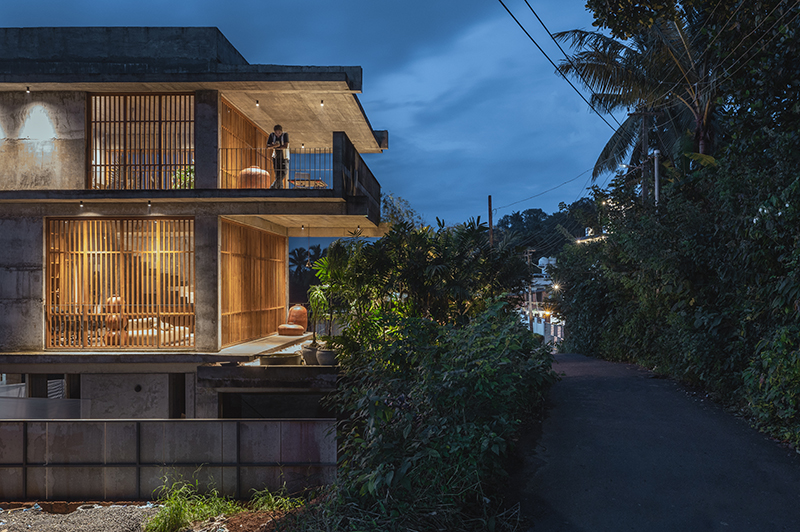 hybrid office-residence extends raw concrete balcony above recessed timber mass in india