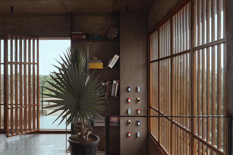 hybrid office-residence extends raw concrete balcony above recessed timber mass in india