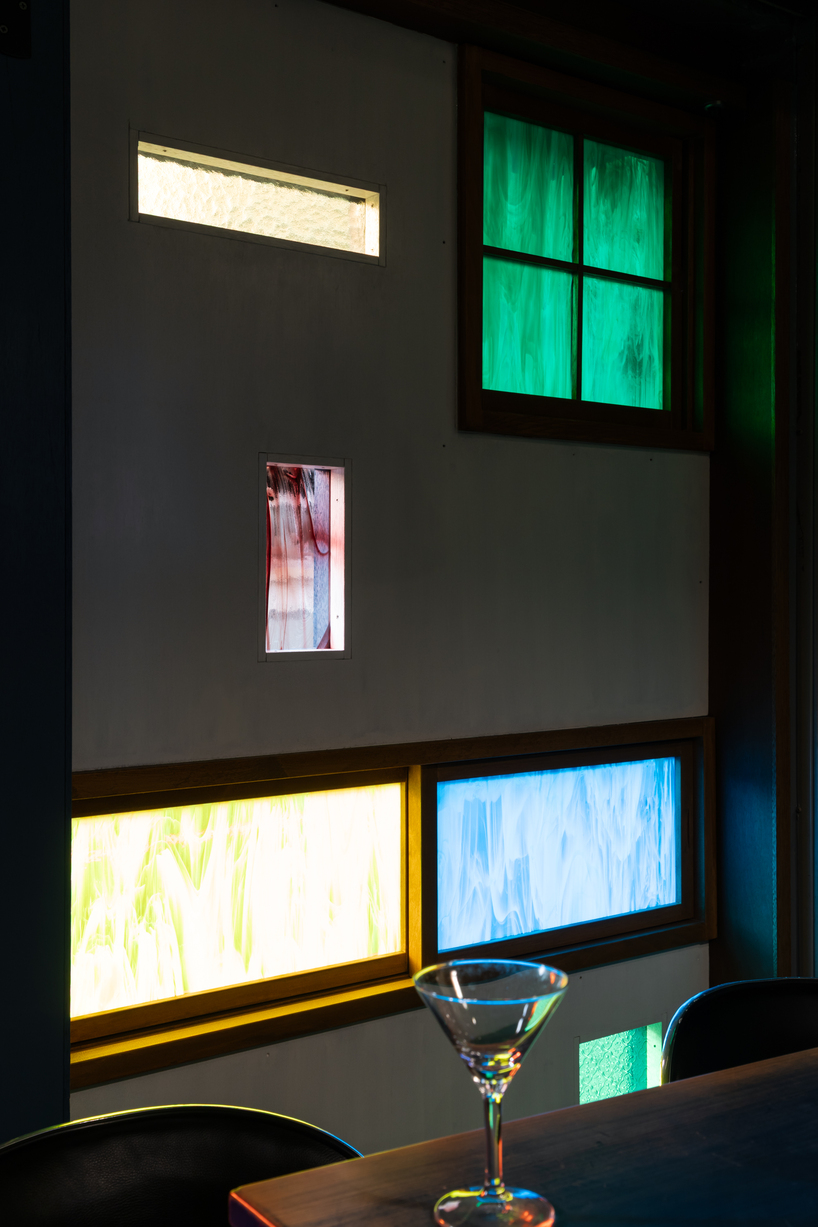 colored glass apertures reveal lively tokyo bar through bright blue entrance