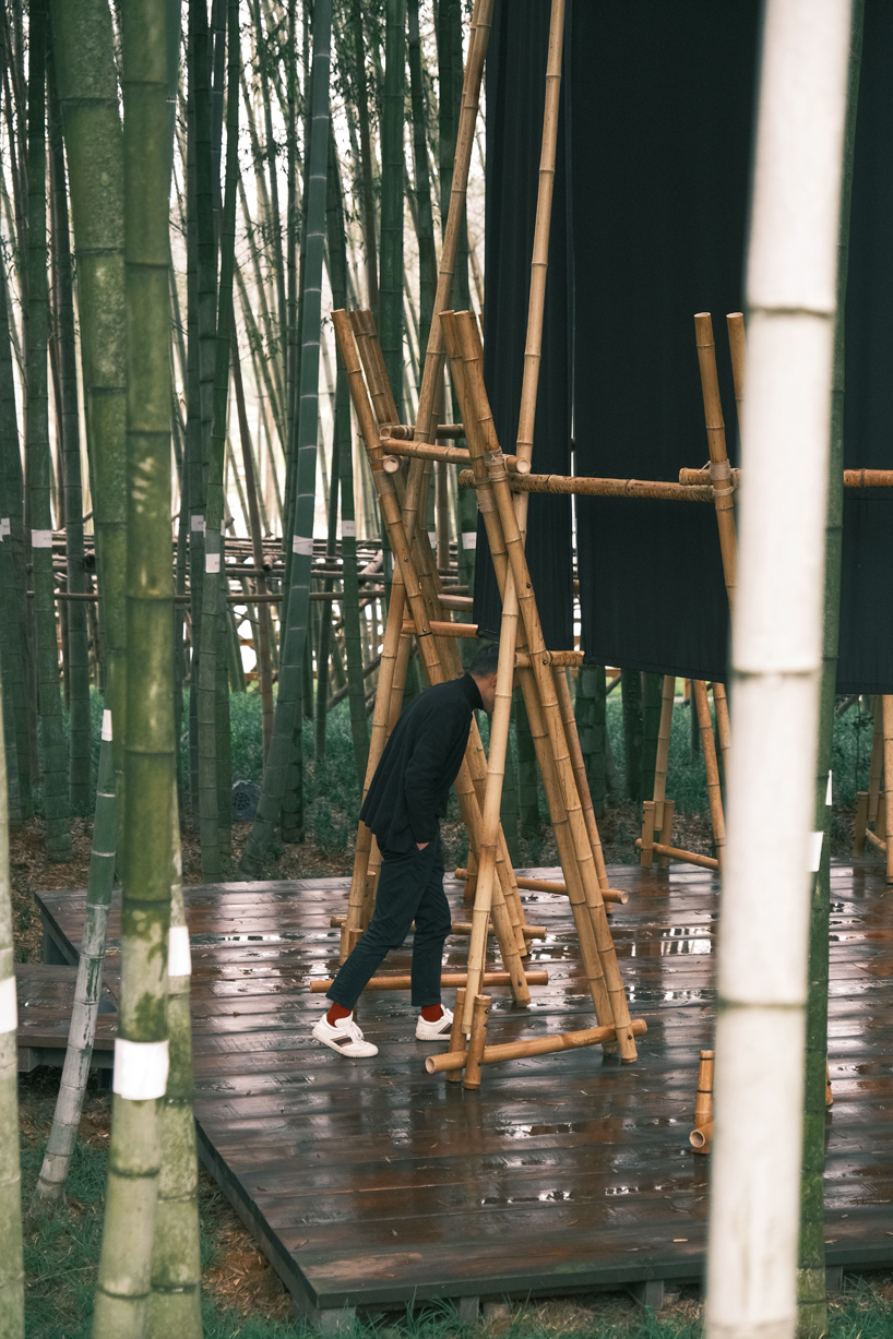 a black fabric veil hovers within a raw bamboo matrix in hubei's dense grove - 8
