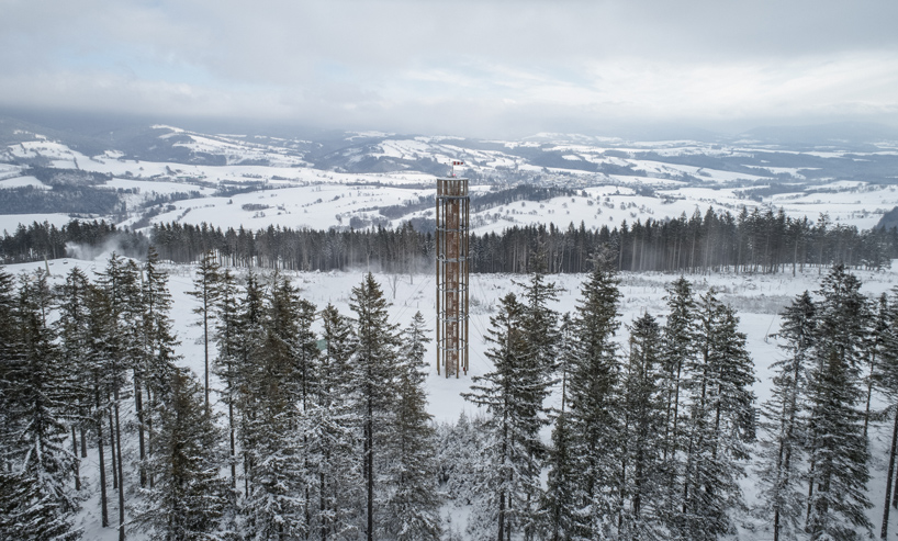 a timber lookout tower rises above the forested mountains of a czech ski area