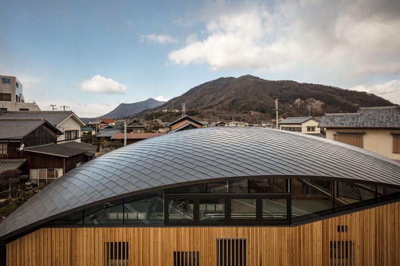 curved wood lattice roof hangs above nasca's blue sky nursery school in japan