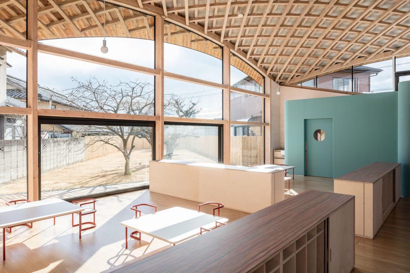 curved wood lattice roof hangs above nasca's blue sky nursery school in japan