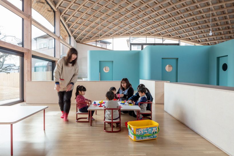 curved wood lattice roof hangs above nasca's blue sky nursery school in japan