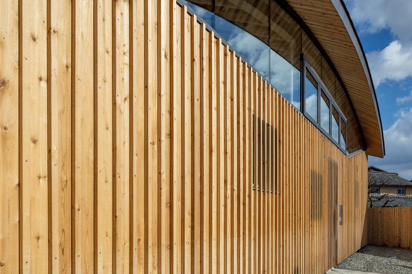 curved wood lattice roof hangs above nasca's blue sky nursery school in japan