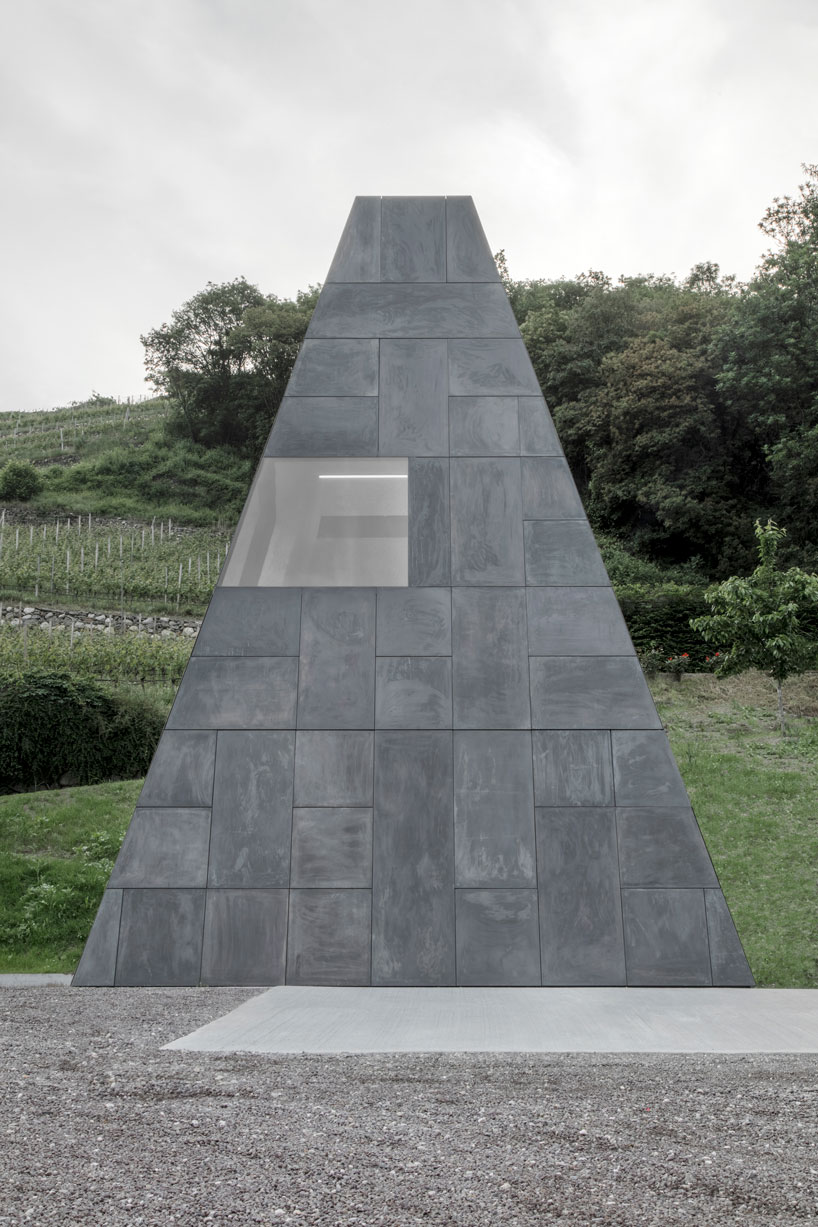 wine cellar in northern italy emerges from ground with stone-like geometry