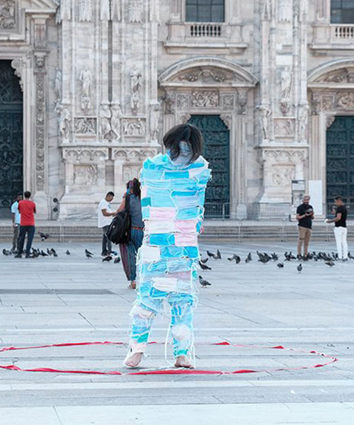 man wrapped by face masks struggles to move in 'no escape' performance in milan, italy