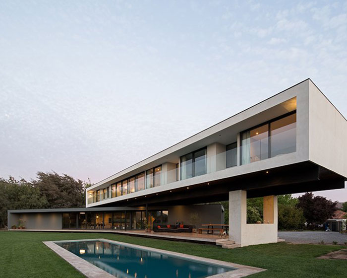 two overlapping elongated concrete volumes form the 'VH' family house in chile