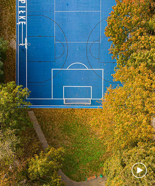 a bright blue sports field designed by UGO hides beneath the trees in poznan