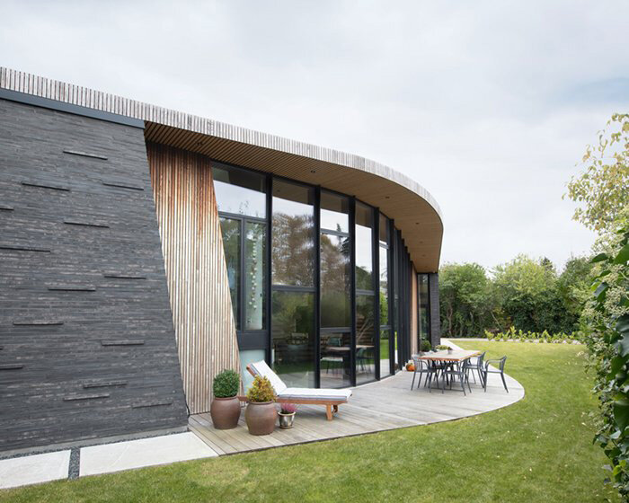 brick volumes + wooden organic cladding form 'boomerang house' by AJG in denmark