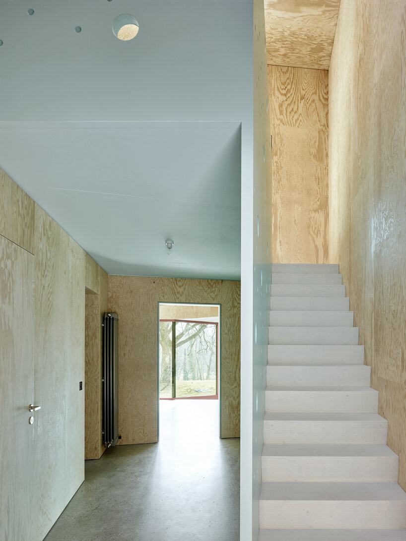 an angular timber house is planned around an old tree in bex, switzerland