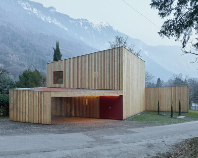 an angular timber house is planned around an old tree in bex, switzerland