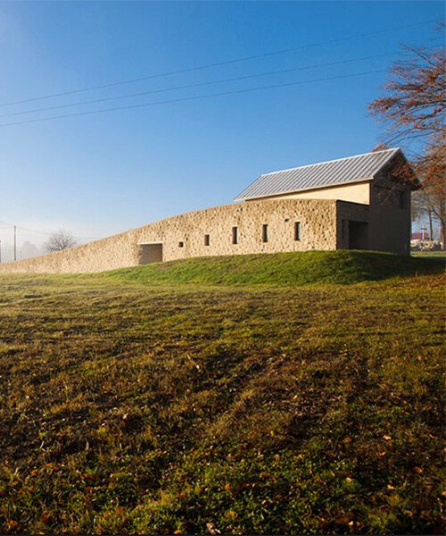 arched stone wall rises from the ground to embrace 'chapel of the last farewell' in poland