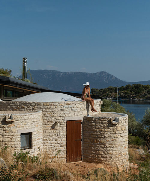 a cluster of curved stone volumes by hiboux architecture nestles in the rocky greek landscape