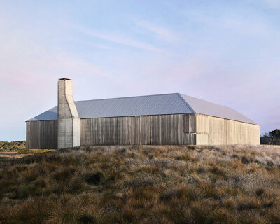 timber-clad 'bass coast farmhouse' cantilevers over rocky sand dunes in australia