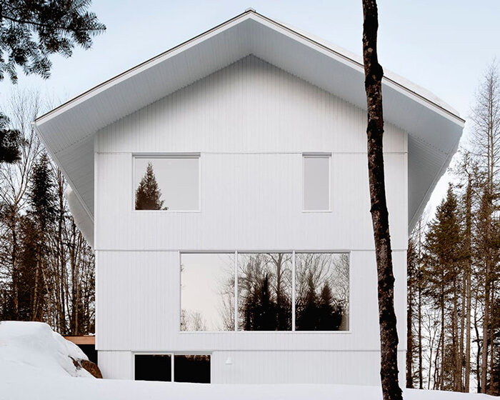 white wooden residence melds with the snowy landscape of quebec's forest