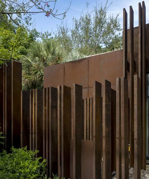 a corten steel gatehouse is overgrown by tropical nature in coconut grove, miami