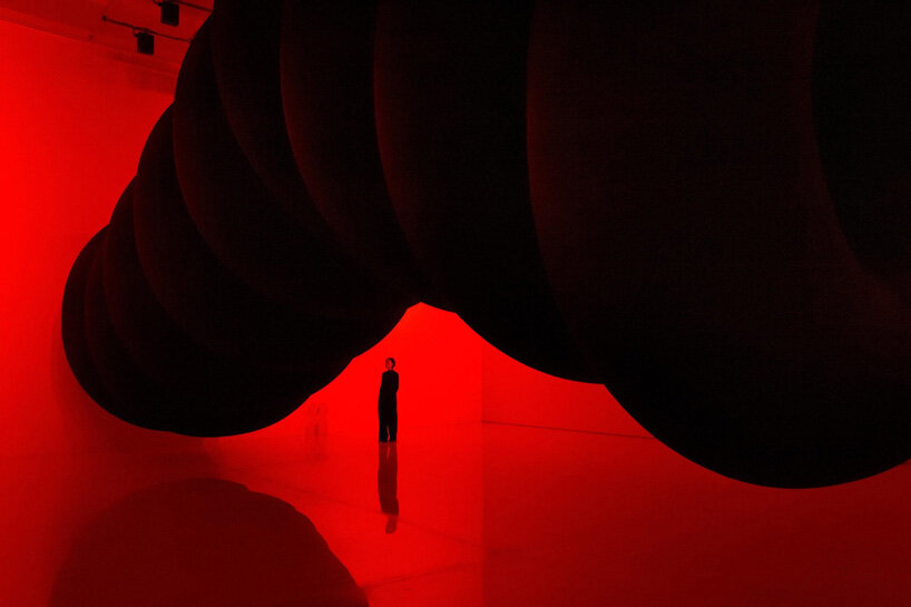 nine colossal tubes undulate and dwarf visitors amid a red glow in SpY's beijing installation