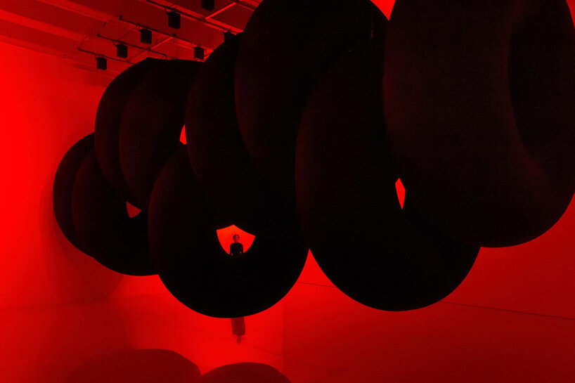 nine colossal tubes undulate and engulf visitors amid a red glow in SpY's beijing installation