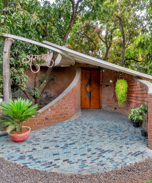 curved brick walls wrap biophilic farmhouse by blurring boundaries in mango grove in india