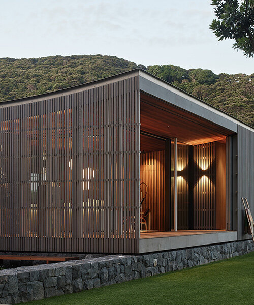 herbst architects' omata beach house glows through a timber screen in new zealand