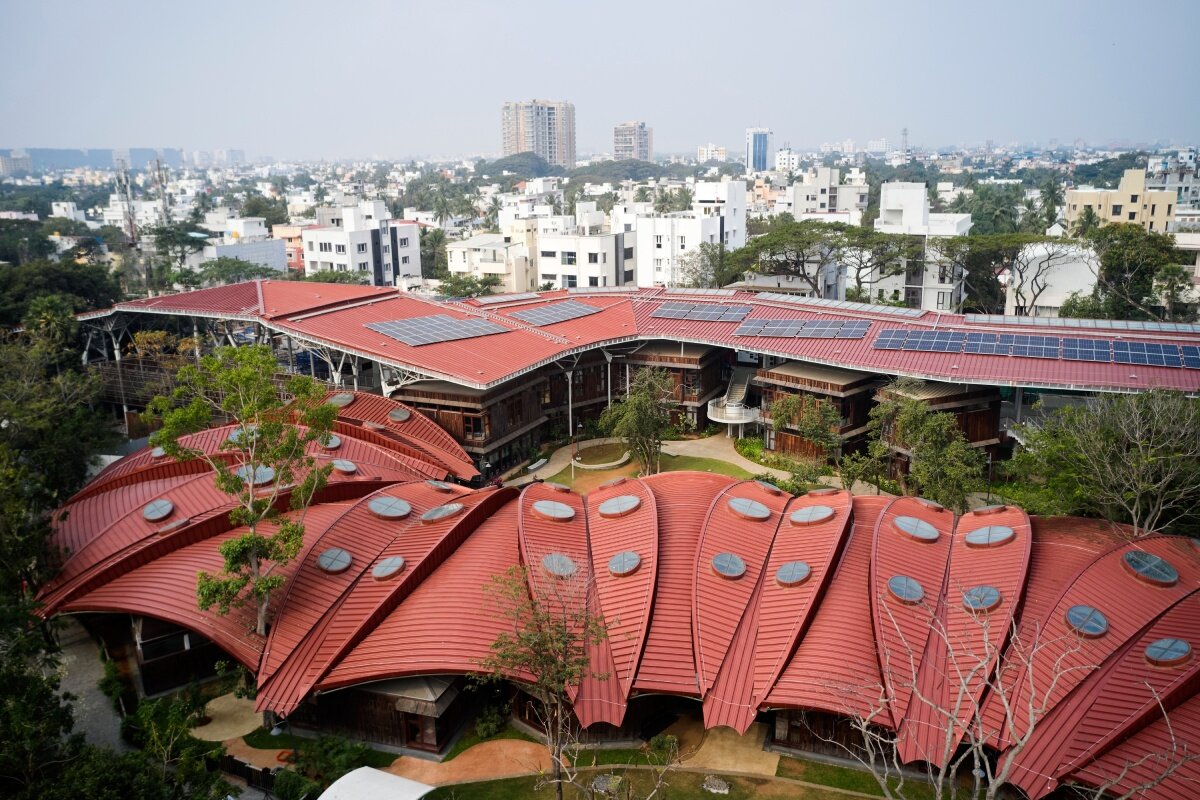layered red roof sweeps over vastushilpa sangath’s tree-filled school in india