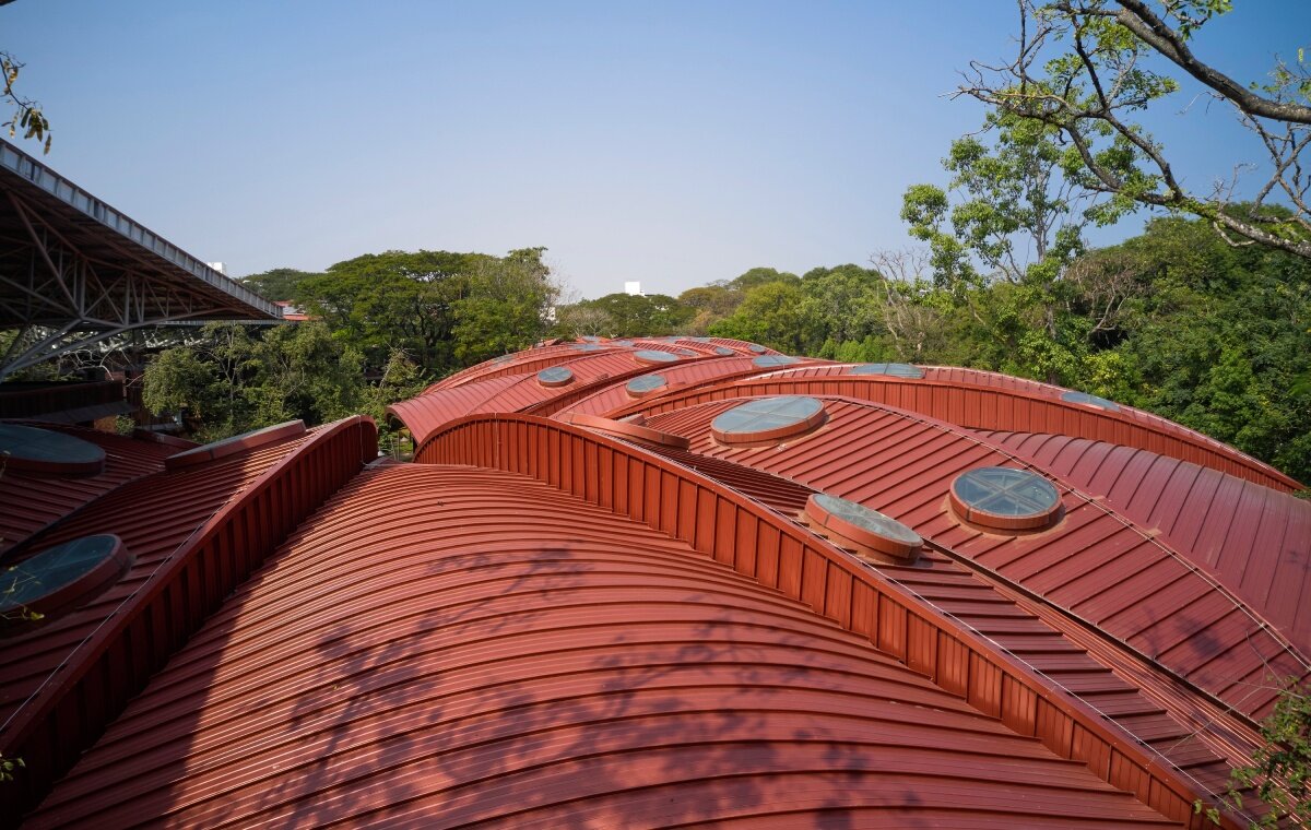 layered red roof sweeps over vastushilpa sangath’s tree-filled school in india
