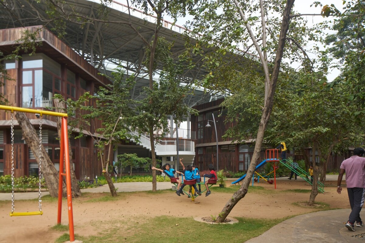 layered red roof sweeps over vastushilpa sangath’s tree-filled school in india