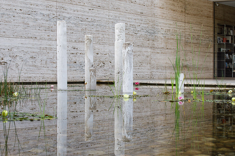 concrete sculptures surface from the pond of mies van der rohe's barcelona pavilion