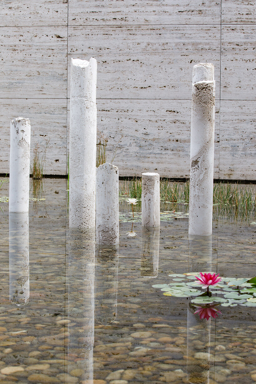 concrete sculptures surface from the pond of mies van der rohe's barcelona pavilion