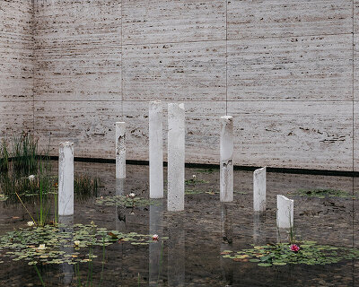 concrete sculptures surface from the pond of mies van der rohe's barcelona pavilion