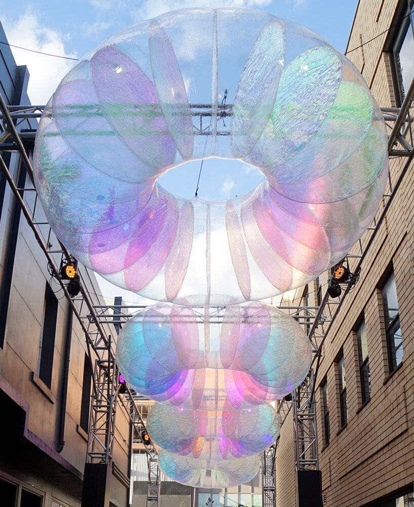 floating oculus installation shimmers in shifting chromatic light above brooklyn's streets