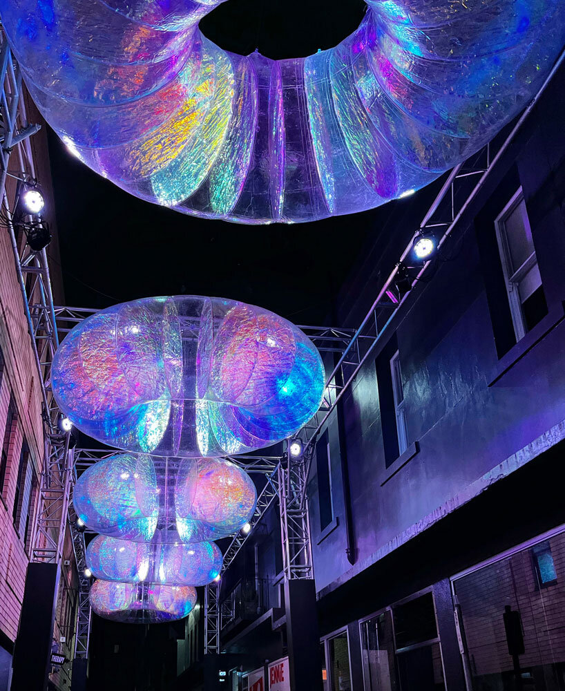 floating oculus installation shimmers in shifting chromatic light above brooklyn's streets