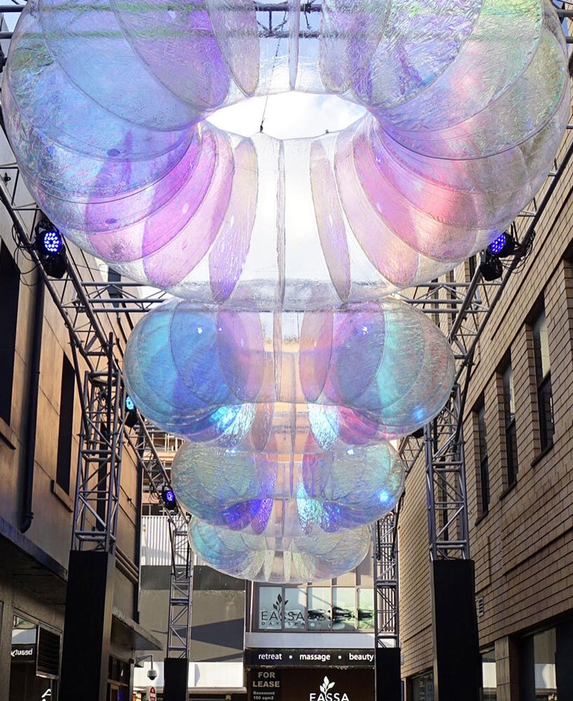 floating oculus installation shimmers in shifting chromatic light above brooklyn's streets